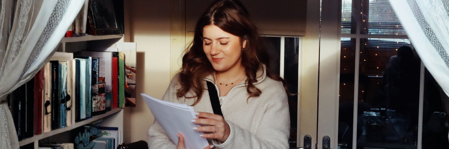 Female student Clara holding a notebook inside a living room 