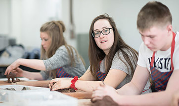 Close up of a row of students with aprons on moulding clay