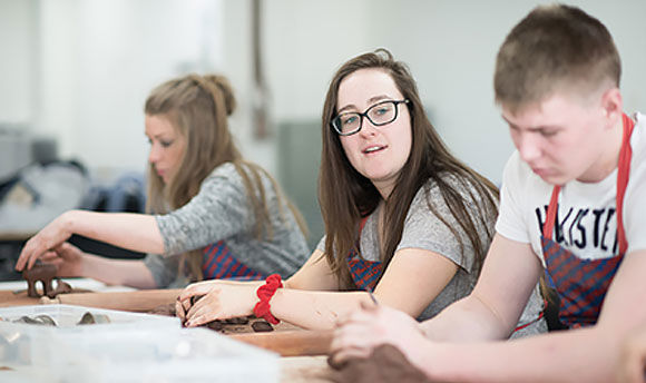 Close up of a row of students with aprons on moulding clay