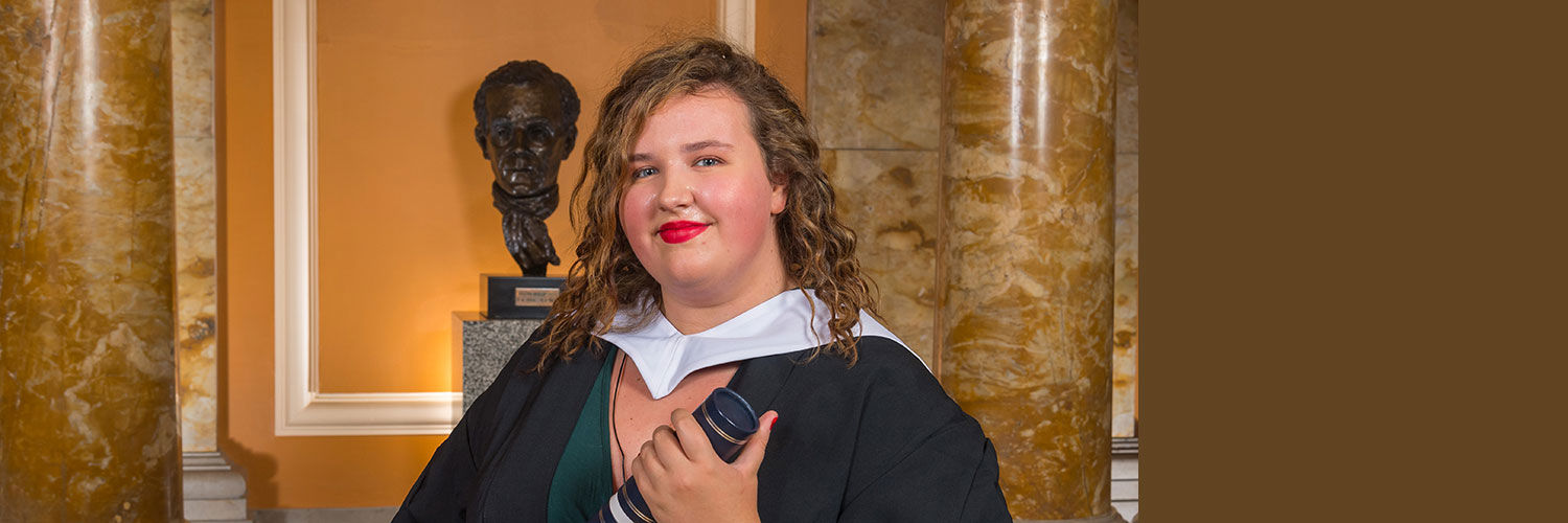 Portrait shot of Rebecca Lannery in her graduation robe holding a graduation scroll