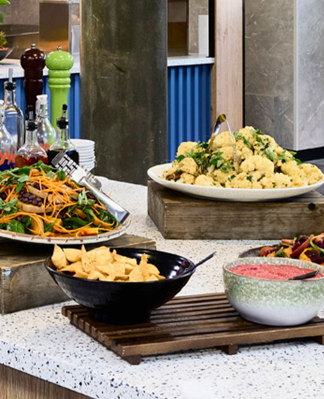 A salad bar featuring a range of dishes, including couscous, vegetables, pasta salad, salad greens, and sauces and dips.