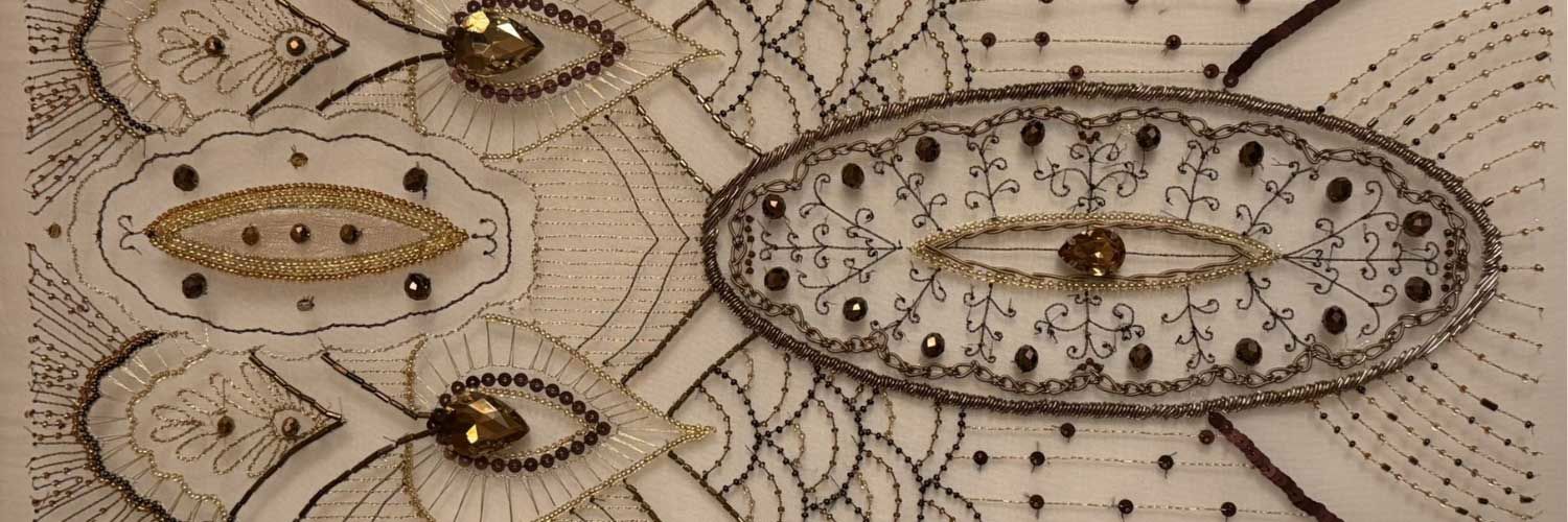 A close up of a hand-embroidered piece of fabric. The item is cream in colour, while the beads are a variety of shades including gold, brown, and black.