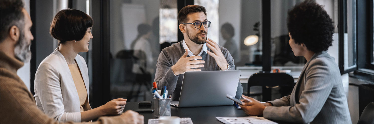 A group of working professionals sit at a meeting table having a lively discussion.