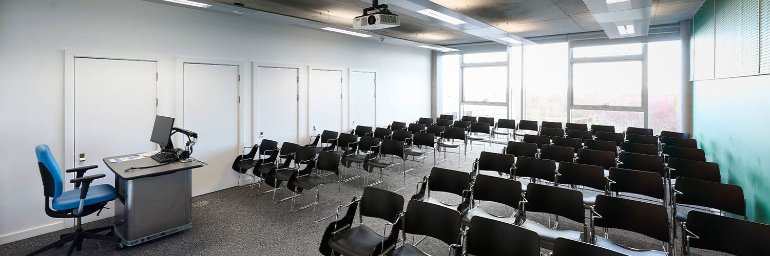 A standard seminar room on Queen Margaret University campus, several rows of chairs with attached desktops fill the room.
