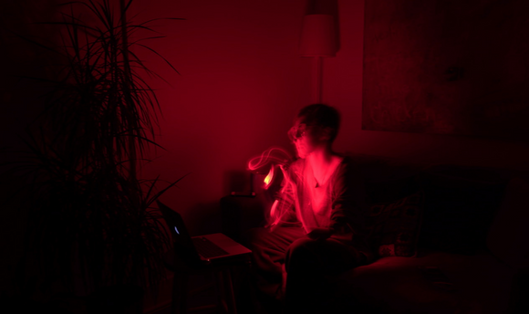 A person lit by red light sitting on a couch in front of a laptop