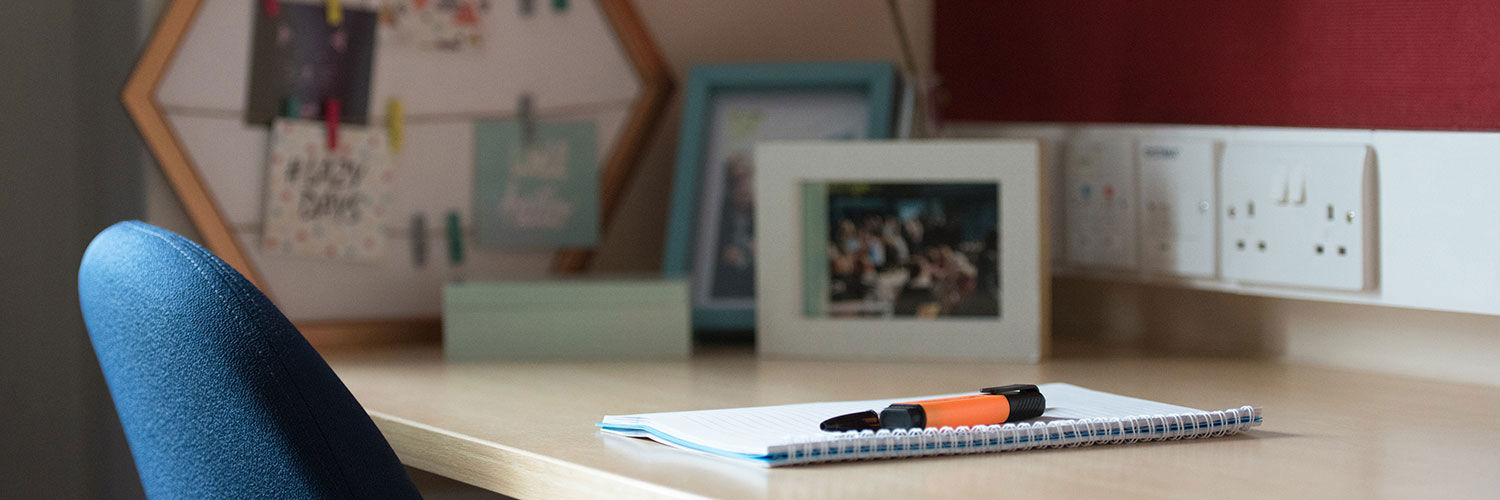 A student accommodation desk with some photographs and a notebook on it