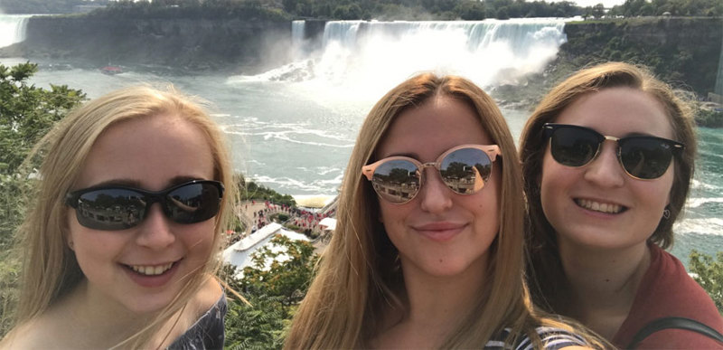 Three people pose for a photograph in front of a waterfall.