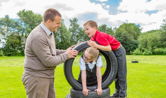 Two children and an adult playing outside with a rubber tyre