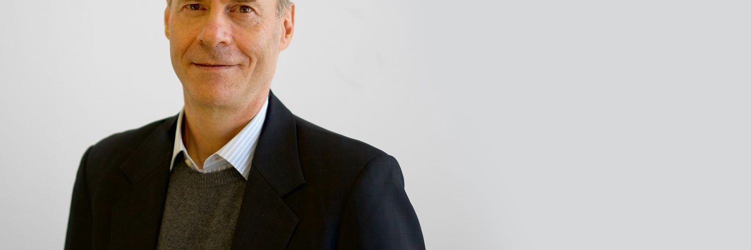 close up image of Daniel Reidpath wearing a suit jacket and shirt with a plain background
