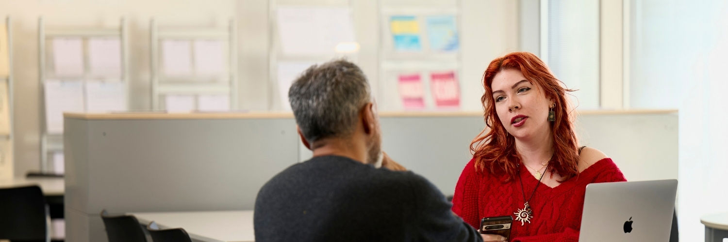 female student with red hair interacting with a male member of staff