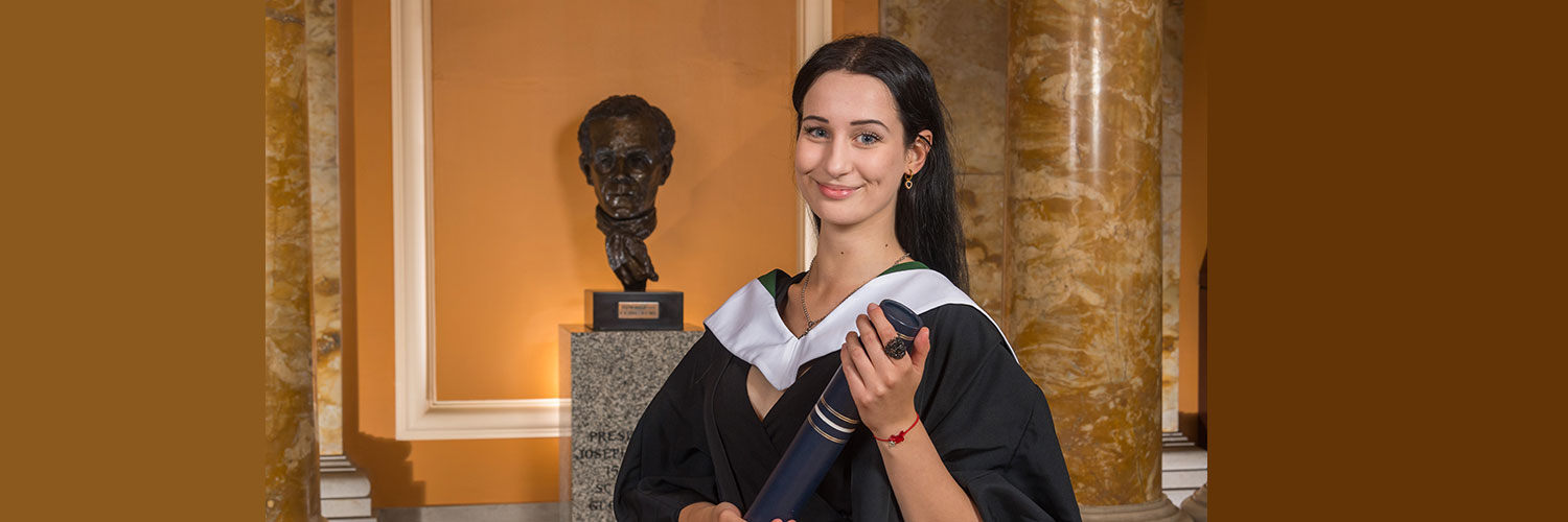 Portrait shot of Leona wearing her graduation gown and holding her graduation scroll