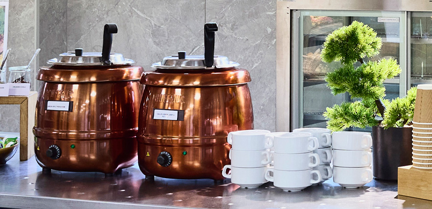 Two copper-toned soup tureens sat atop a counter alongside a stack of bowls.