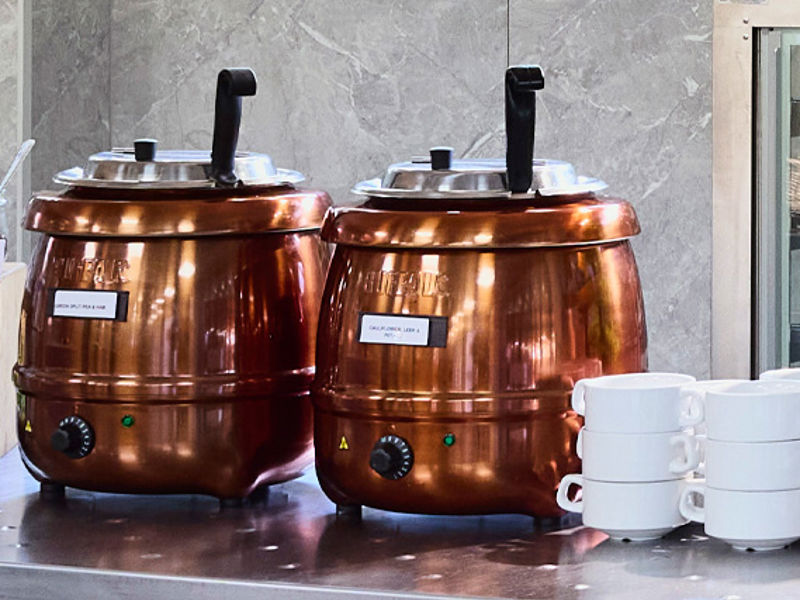 Two copper-toned soup tureens sat atop a counter alongside a stack of bowls.