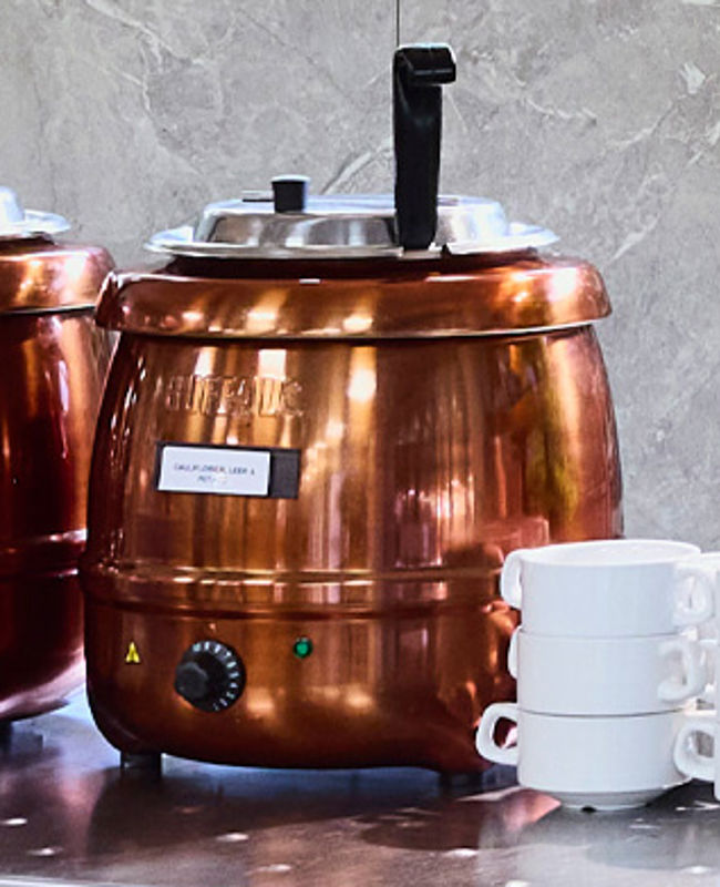 Two copper-toned soup tureens sat atop a counter alongside a stack of bowls.
