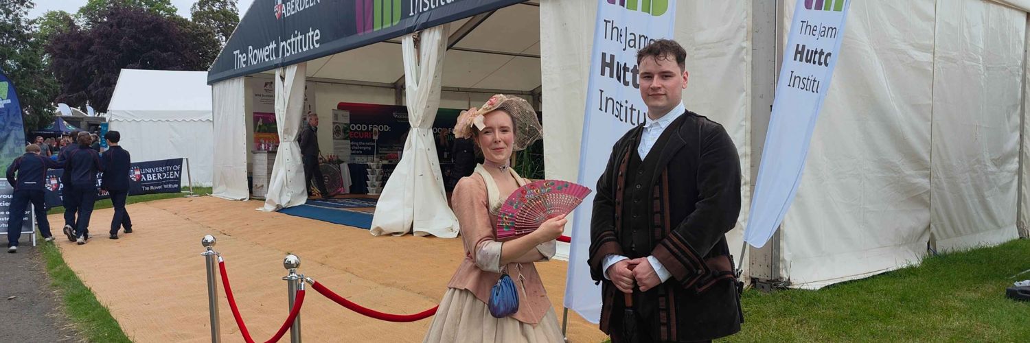 one male and one female student dressed in period costumes with backdrop of Highland Show marquee