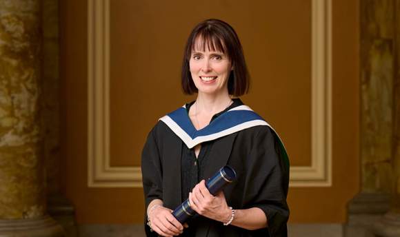 portrait shot of female with bobbed hair smiling and wearing her graduation robe