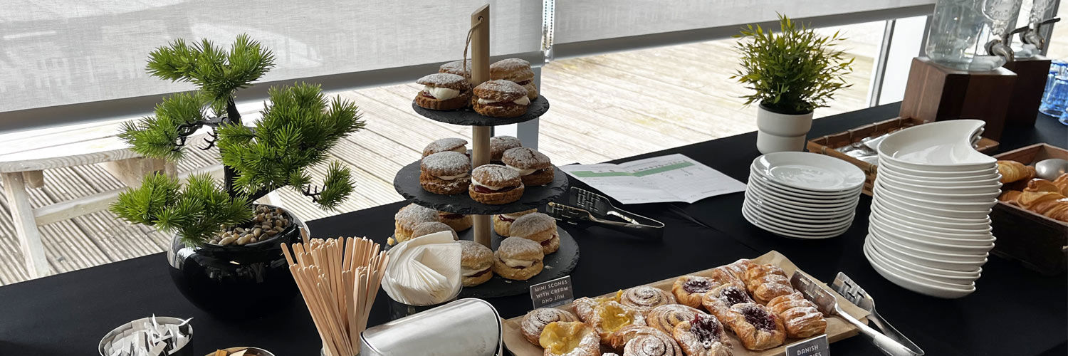 A table filled with pastries, tea and coffee, plates, and other serveware items.