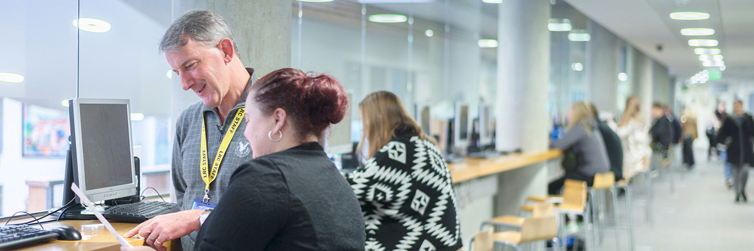 A man wearing a bright yellow assistance lanyard helps a woman with her laptop.