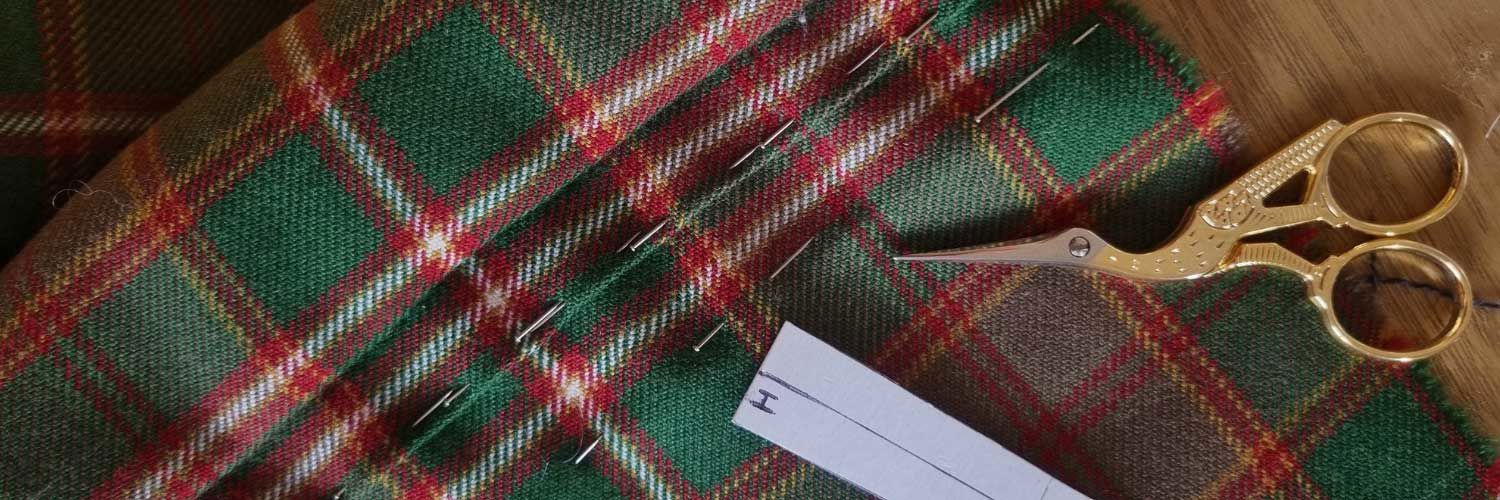 A rich green and red tartan sits on a table alongside some sewing scissors.