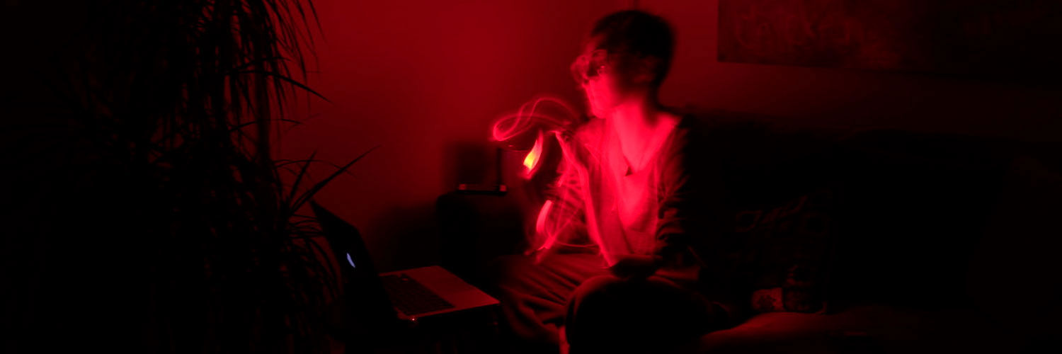 A person lit by red light sitting on a couch in front of a laptop