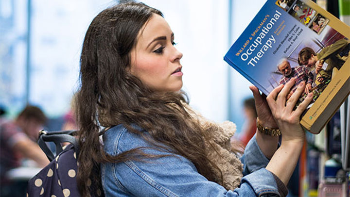 A student pulling an occupational therapy book out of a library bookshelf