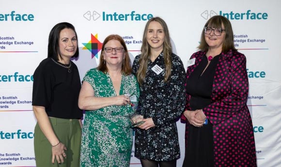 Four people pose for a photograph, holding an award won at the Interface Awards.