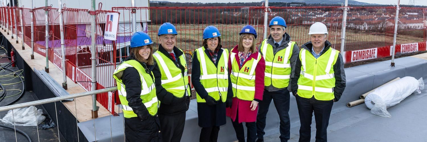 A group of people wearing hard hats and high-vis vests on top of a building.