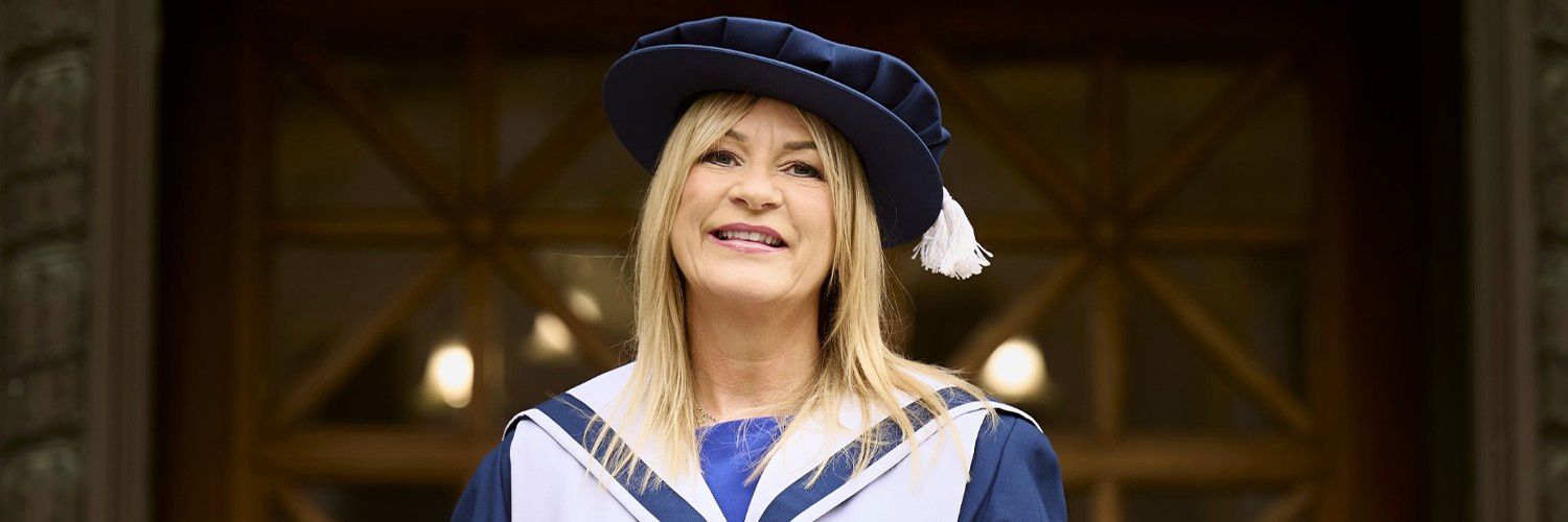 Sally Gray in her graduation gown  in front of a glass framed wooden door
