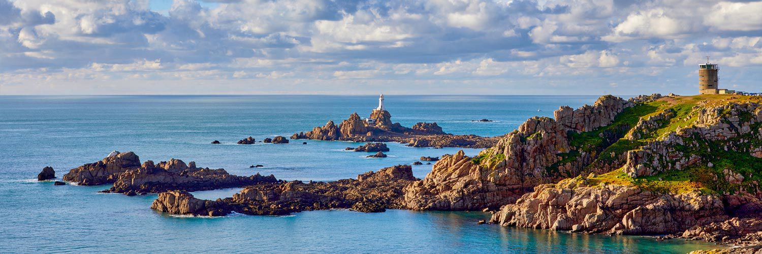 Corbiere lighthouse with WW2 tower, coastline and calm sea.