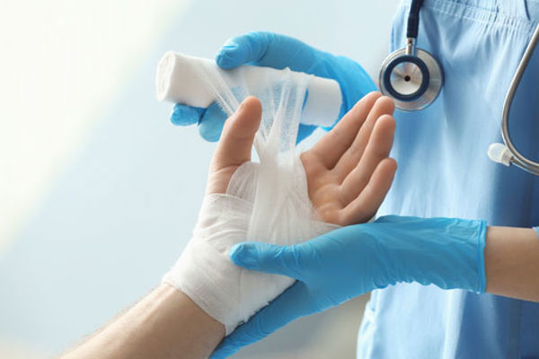 A nurse wraps a gauze dressing around a patient's hand and wrist. 