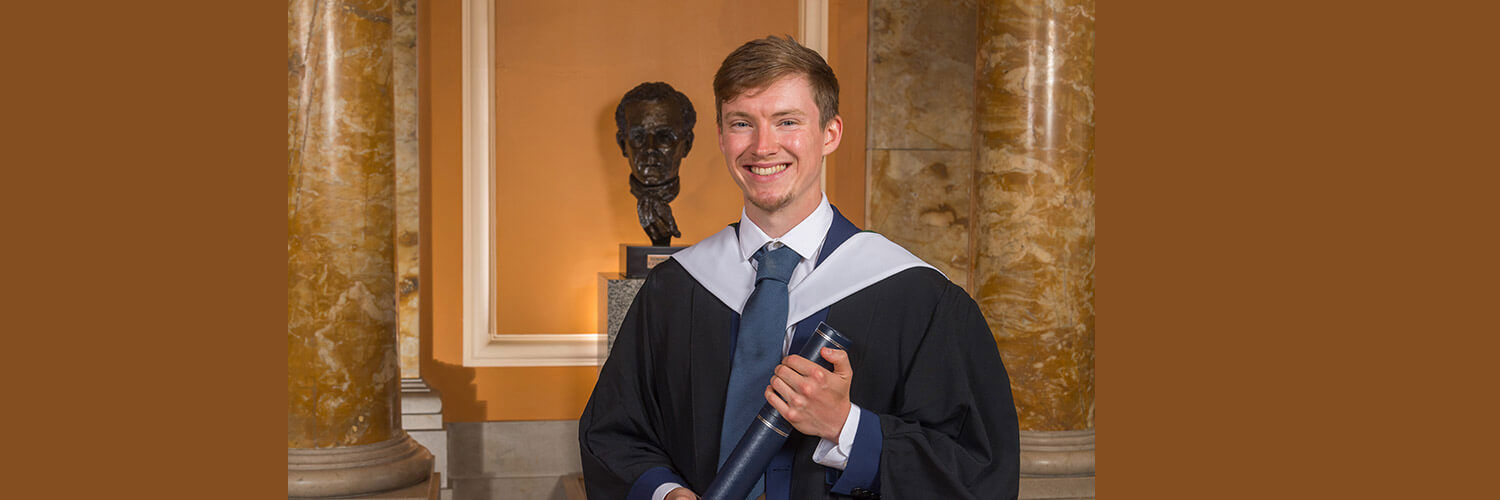 Formal image of young man wearing graduation robes and holding graduation scroll