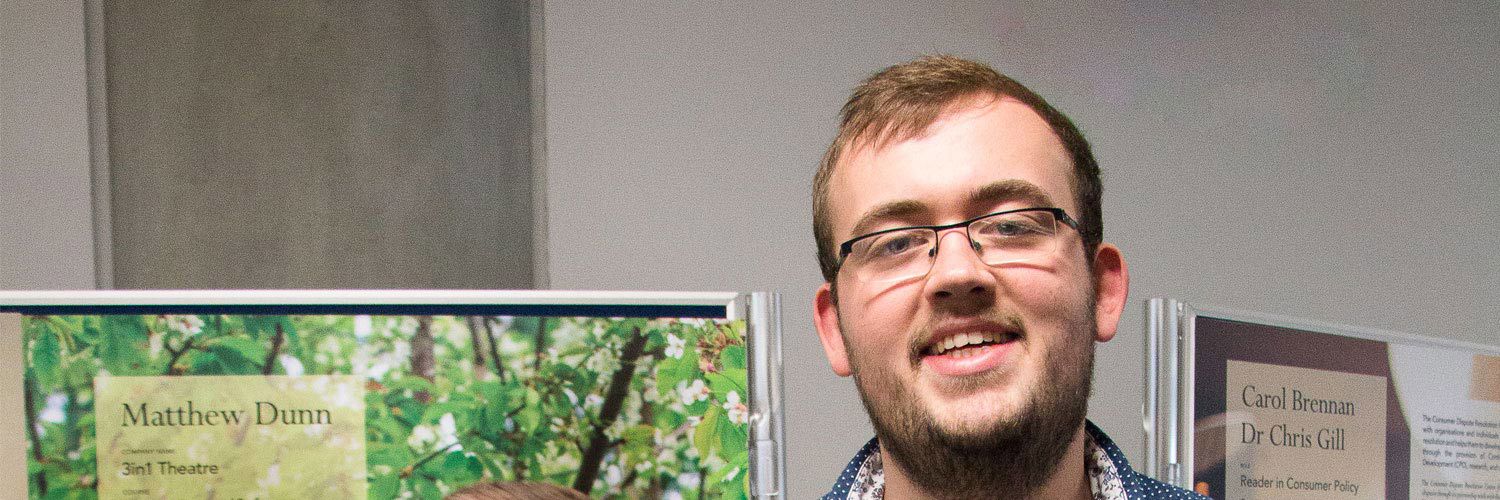Matthew Dunn smiling by a poster with him on it