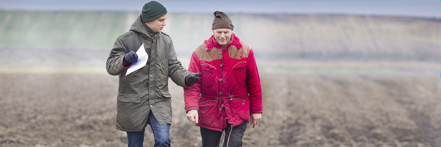 Two men in warm jackets and hats walking through a field