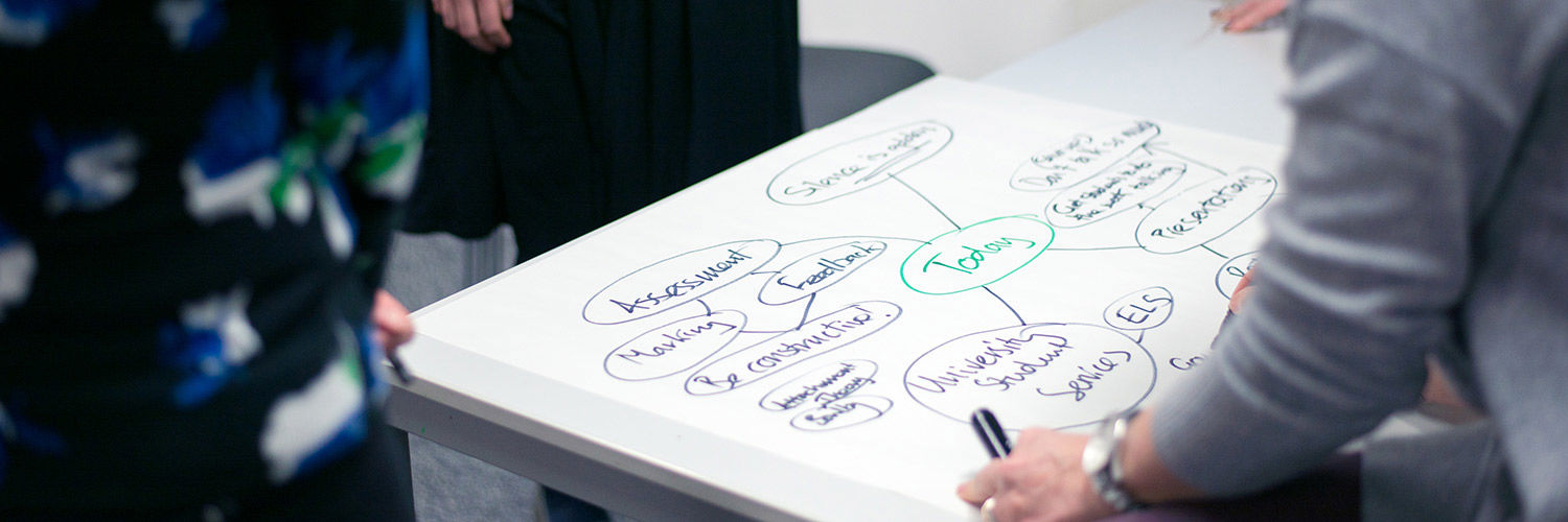 Close up of a woman writing out a mind map whilst others stand round the paper