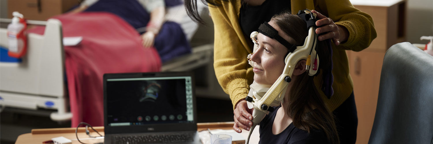 A member of the research team adjusts the ultrasound headgear worn by another person.