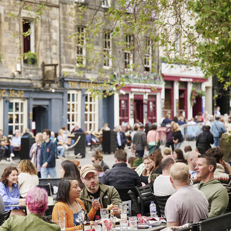 A crowd of people enjoying food and drinks in the sunshine in Edinburgh's Grassmarket
