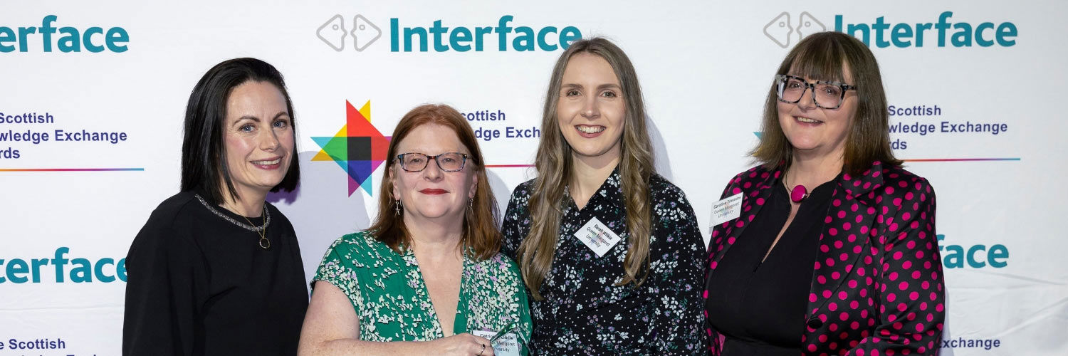 Four people pose for a photograph, holding an award won at the Interface Awards.