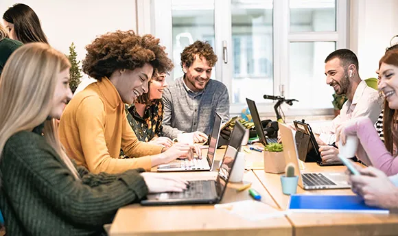 Group of colleagues sitting around a table chatting with laptops