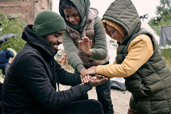 A man and two boys wearing warm clothing and hats, they are playing a hand-clapping game together.