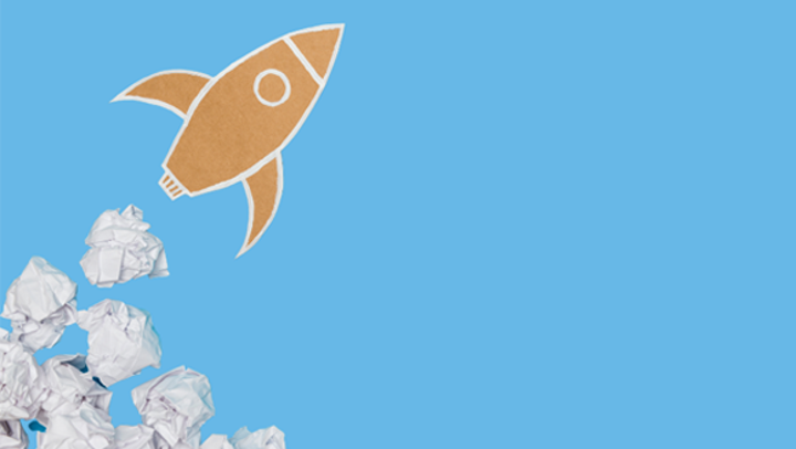 A cardboard rocket launches out of a pile of scrunched up pieces of paper.