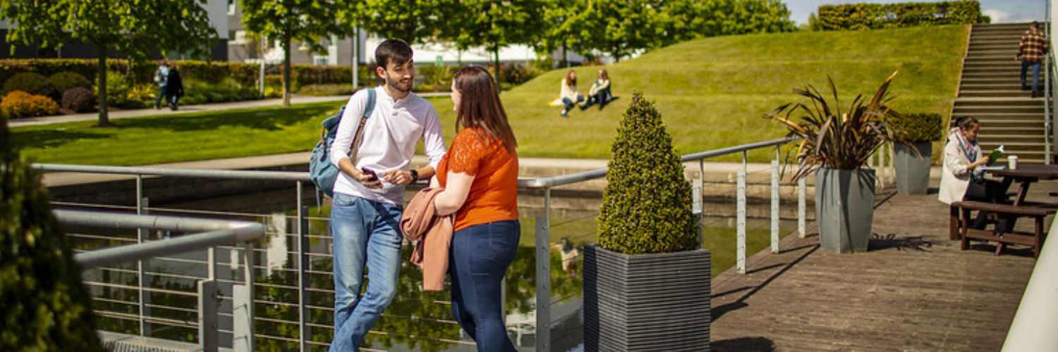 QMU students chatting beside pond on campus grounds